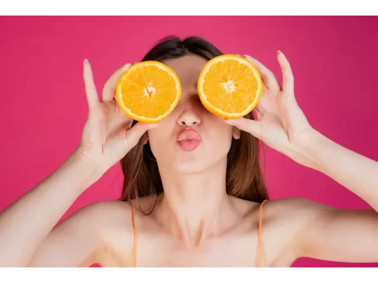Melyik a legjobb C-vitamin? Fiatal nő bohókásan a szemei elé helyez egy-egy fél narancsot