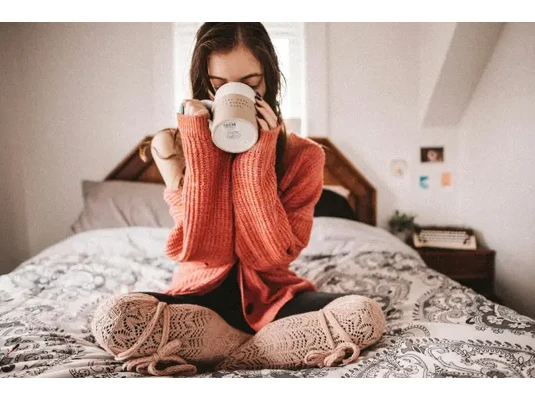 Fiatal nő ágyon ülve teázik - Mályva tea bélvédő hatásai